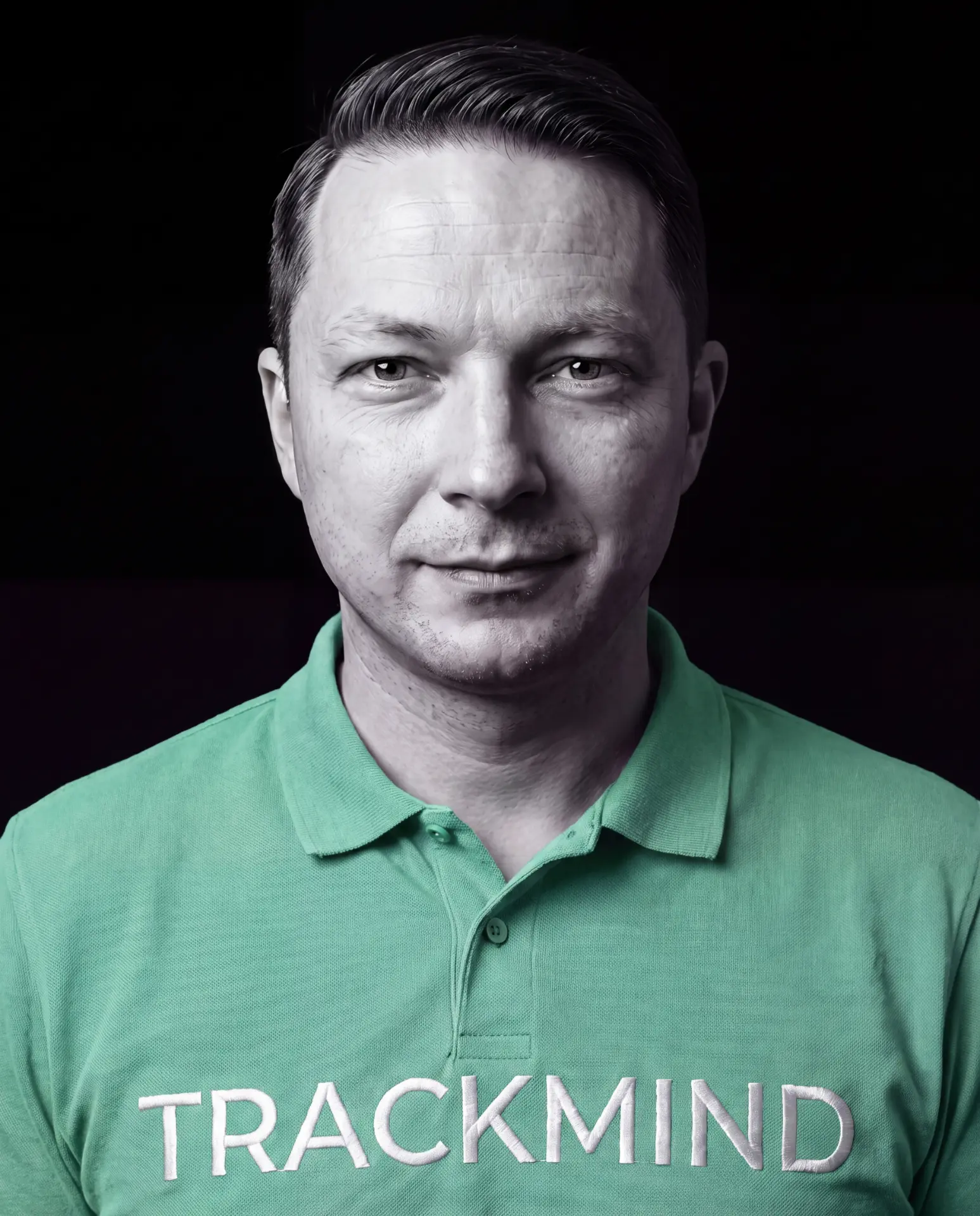 Porträt von Carlo Steckert, Gründer und Mental Performance Coach von TrackMind: kurze dunkle Haare, dunkelgrünes Polohemd mit TrackMind-Stickerei, vor dunklem Hintergrund, ruhiger Blick in die Kamera